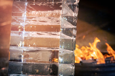 A close up shot of the stacked ice blocks forming the arch. The ice is melting. Flames are burning in the background.