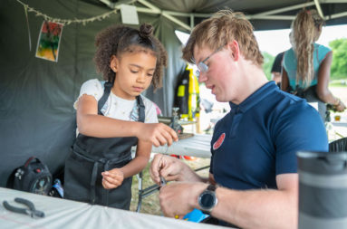 A child and adult work together to cut a piece of wire for the fish mobile take home kit.