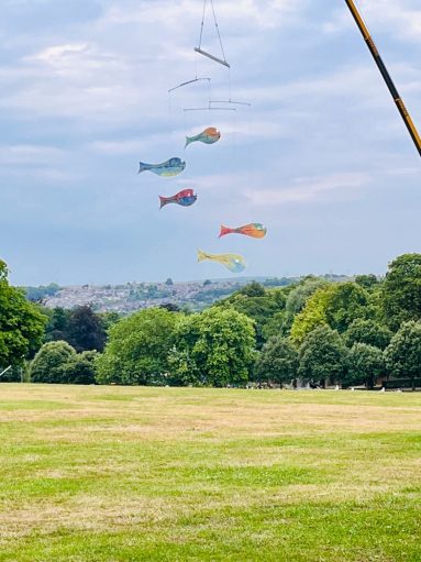 Outdoors. Fish Mobile hangs in the sky above the treeline of Rotherham's Clifton Park.